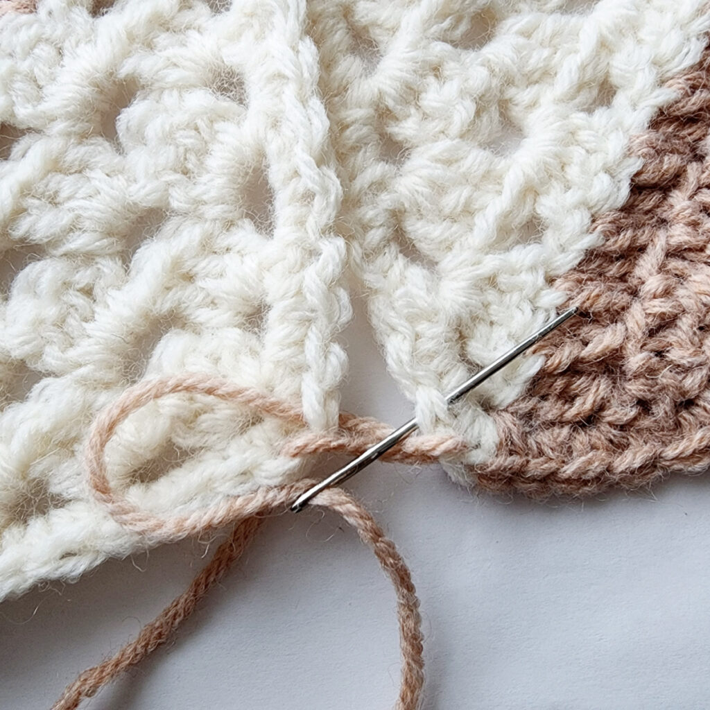 Seaming two crochet granny square motifs with a needle.