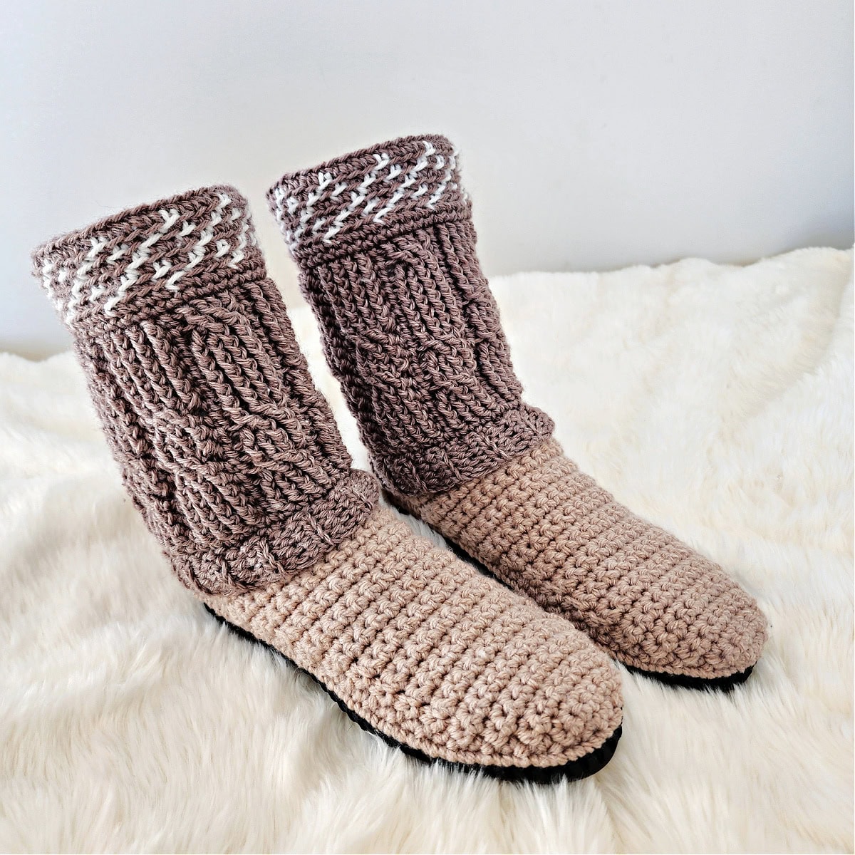 The crochet cable slipper boots on a white sheet.