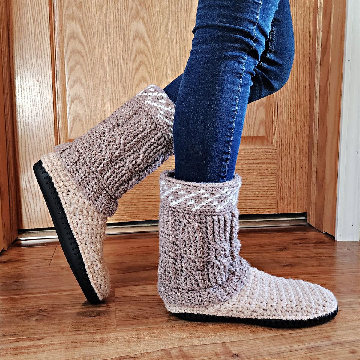 Person wearing blue jeans with a side view of the crochet cable slipper boots on a wooden floor.