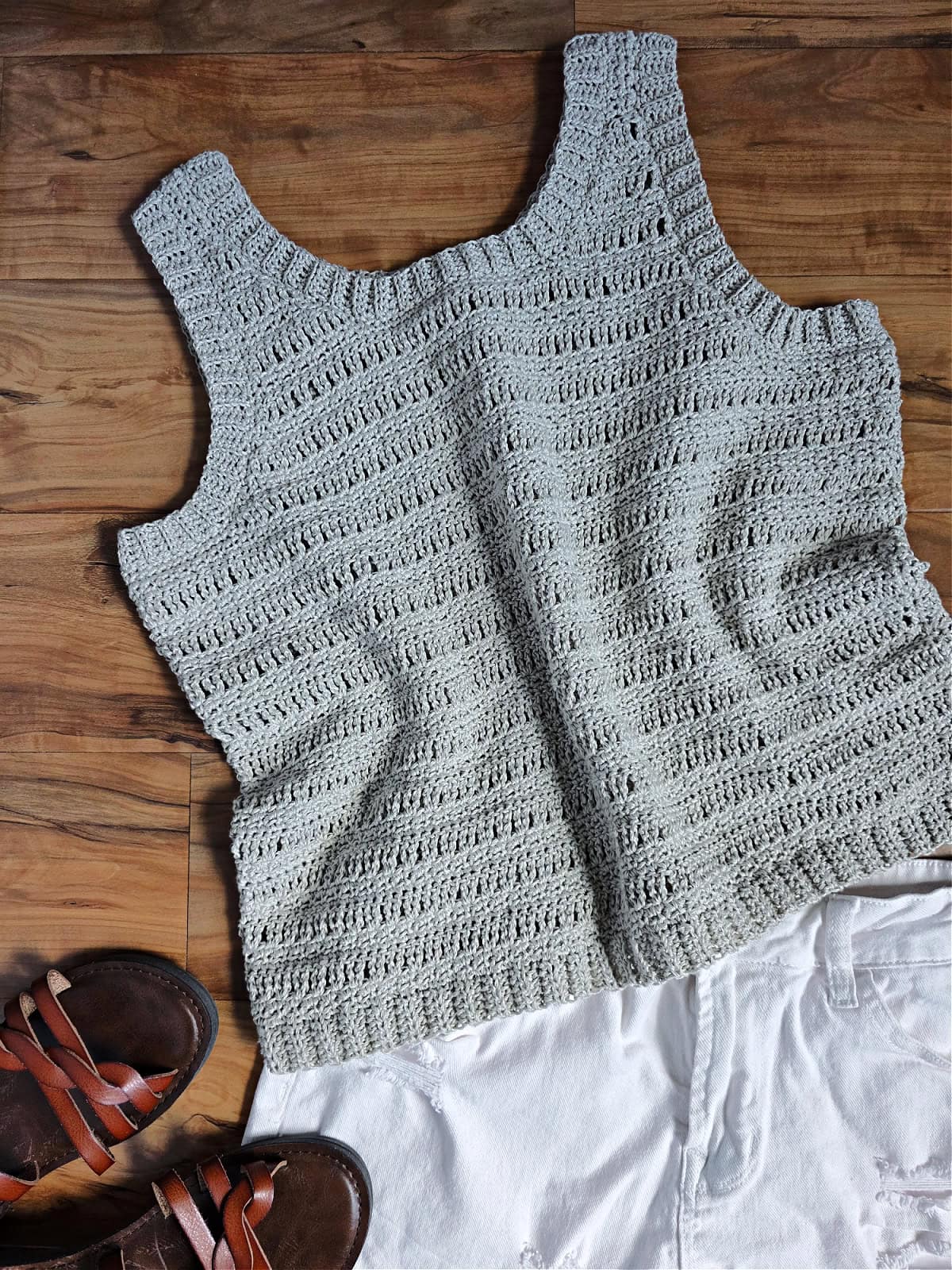 A gray crochet tank top laid against a wooden background next to a white bottom and shoes.