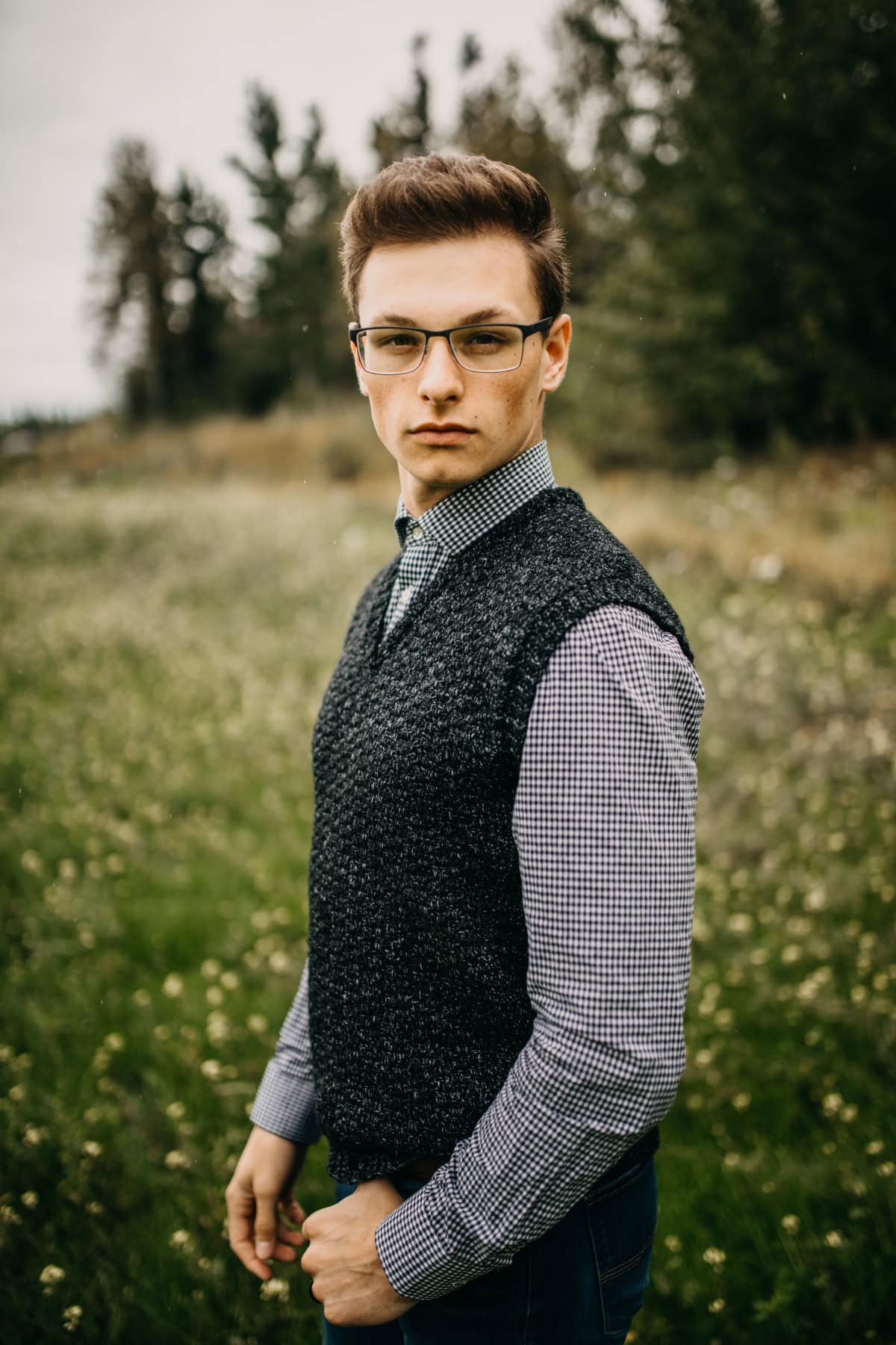 Man standing in a field wearing a dark crochet vest and glasses.