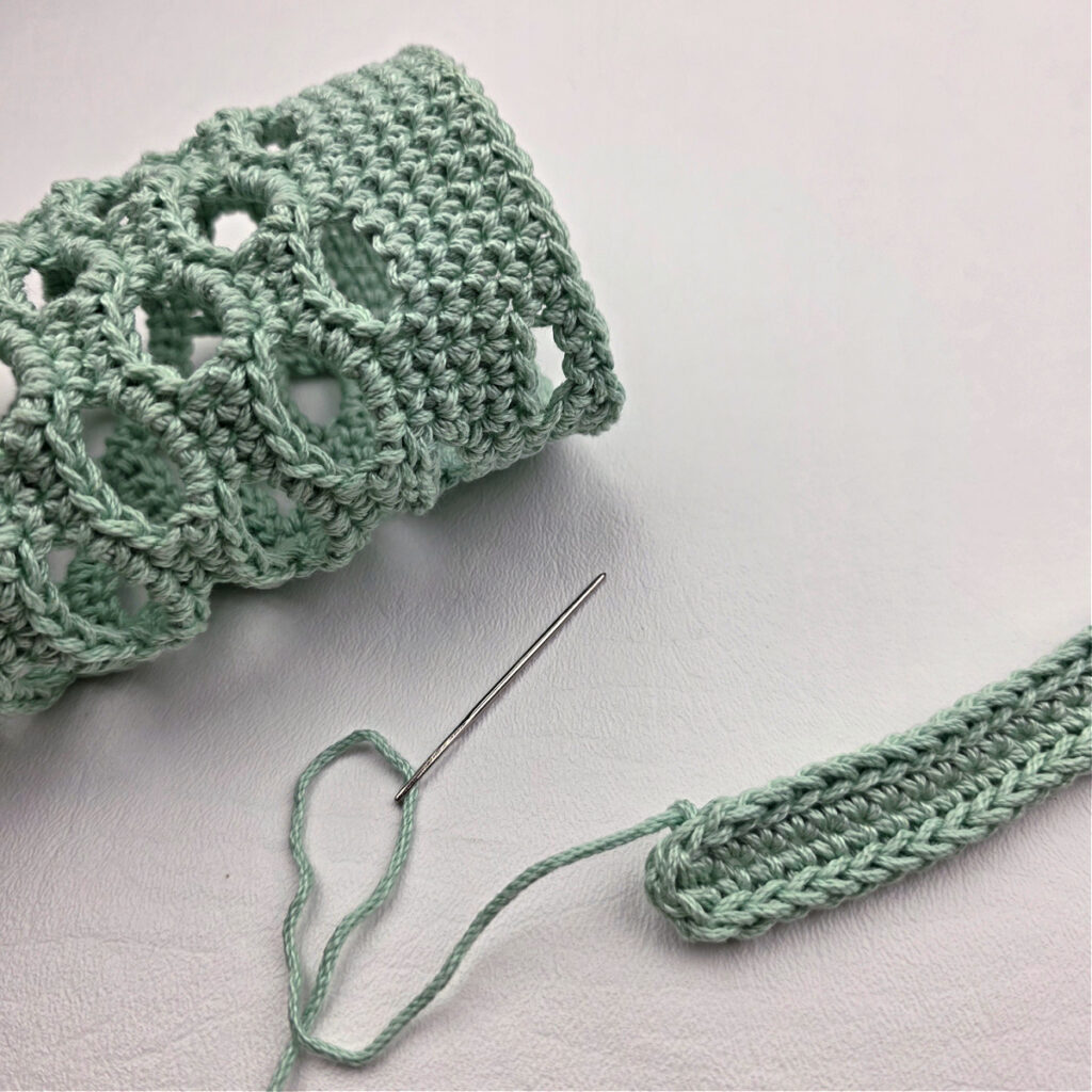 Attaching a mint colored crochet strap to a water bottle holder.