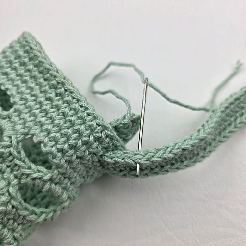 Attaching a mint colored crochet strap to a water bottle holder.