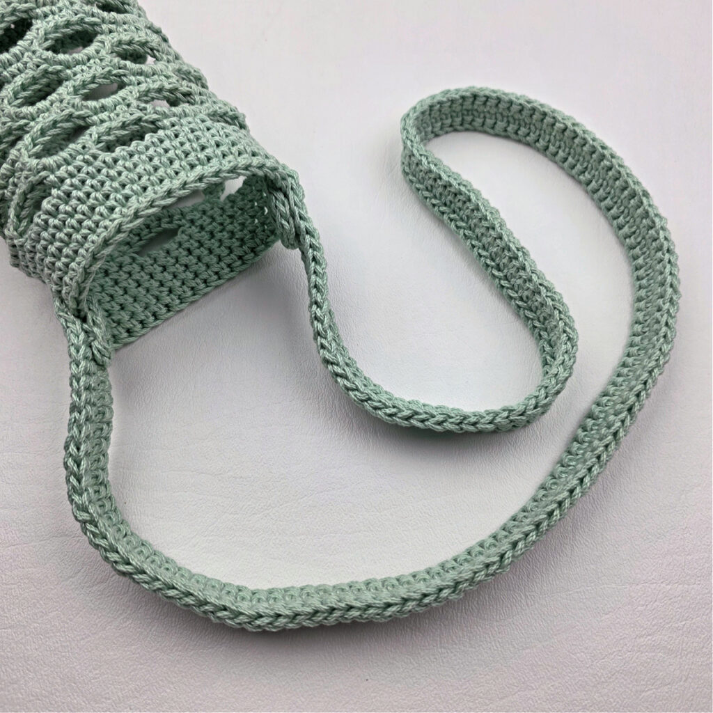 Attaching a mint colored crochet strap to a water bottle holder.