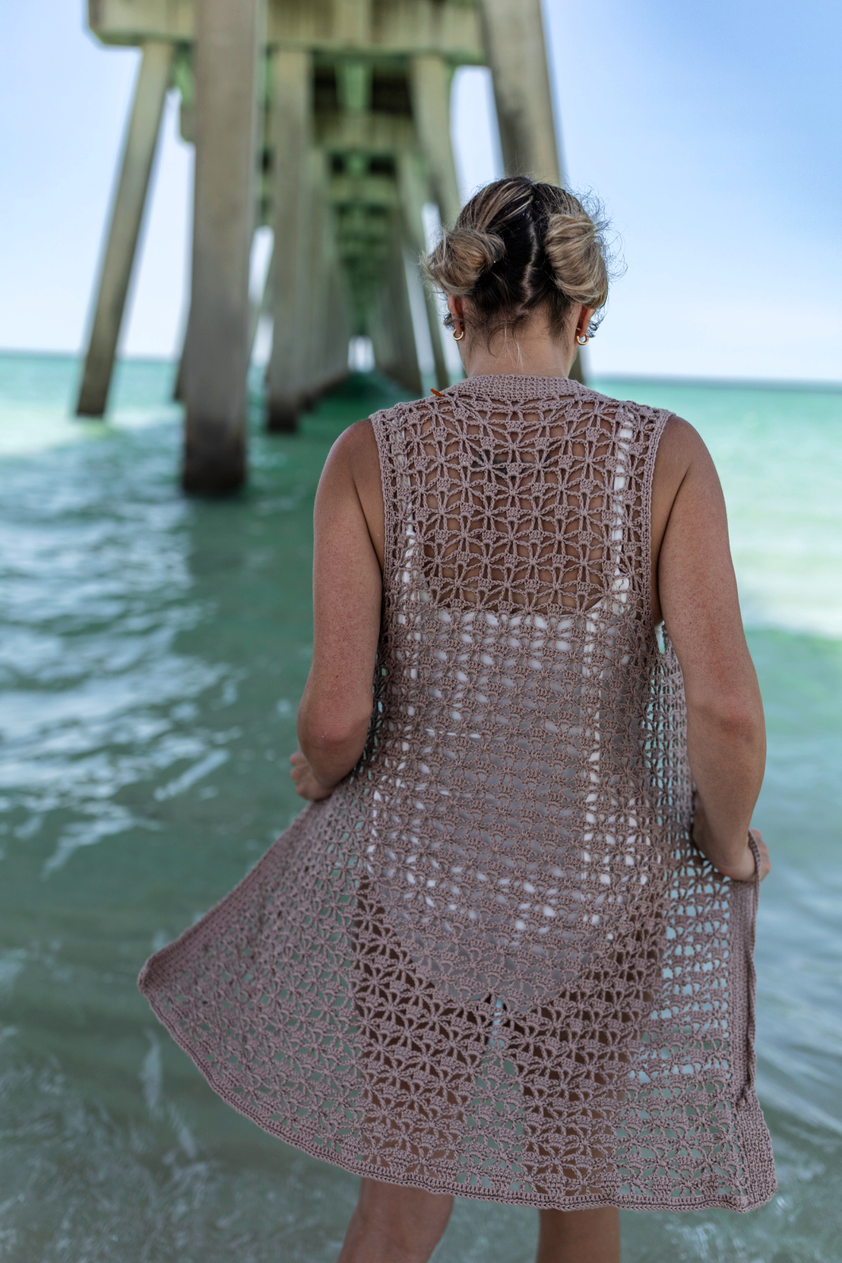 Woman wearing a crochet beach cover-up over a white swimsuit and standing in the ocean.