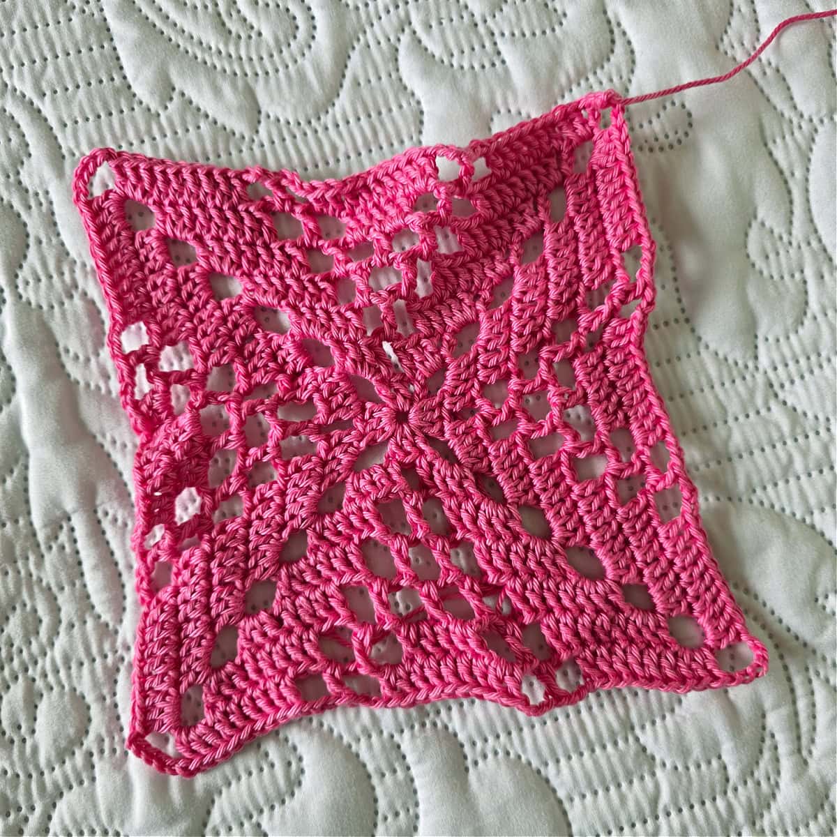 Pink granny square before blocking.