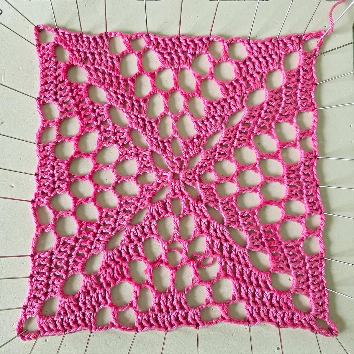Pink granny square pinned on a blocking board.