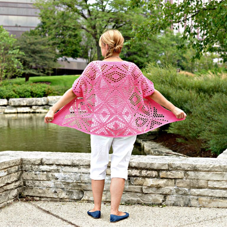Woman standing in front of a stone wall with her back to the camera wearing a pink lacy cardigan.