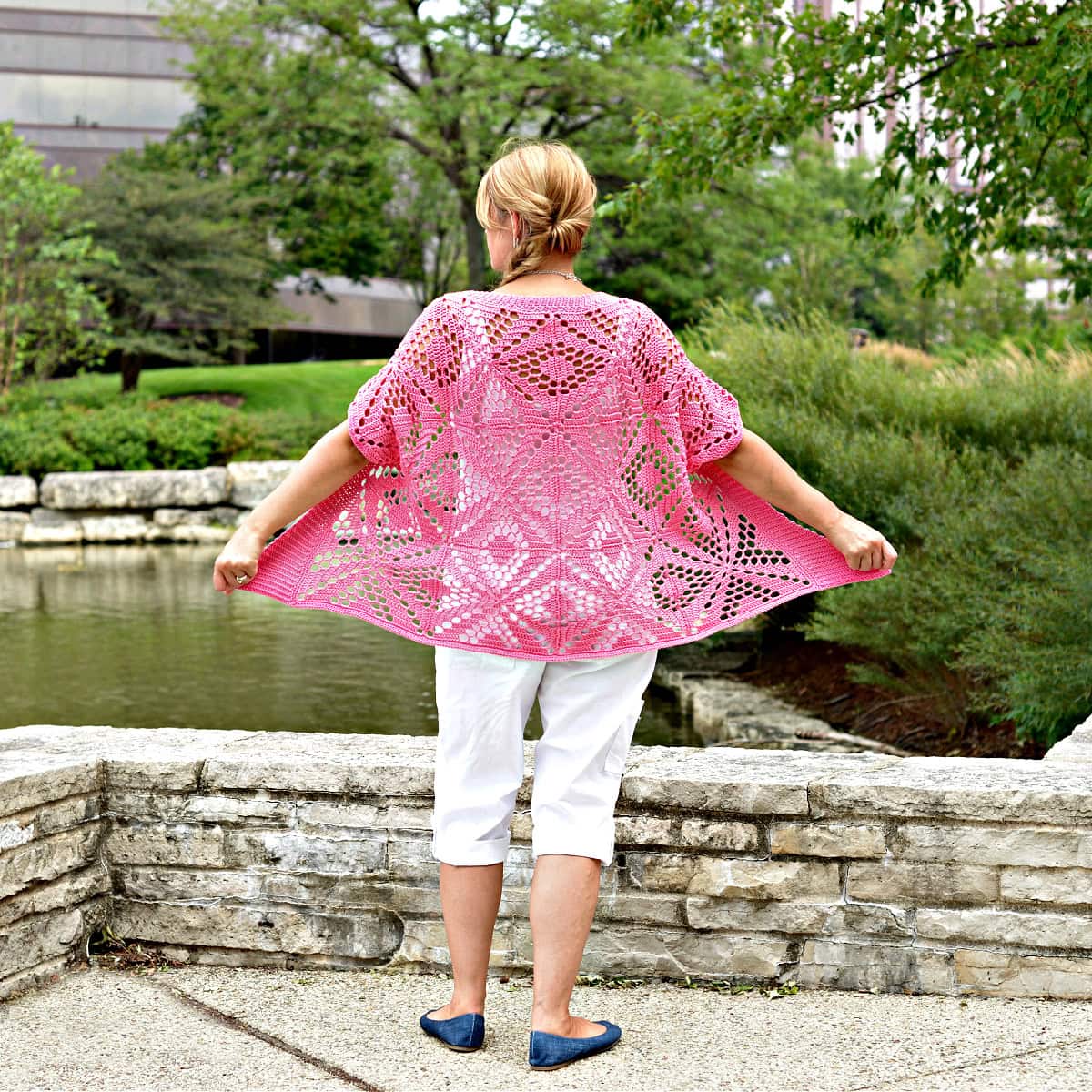 Woman standing in front of a stone wall with her back to the camera wearing a pink lacy cardigan.