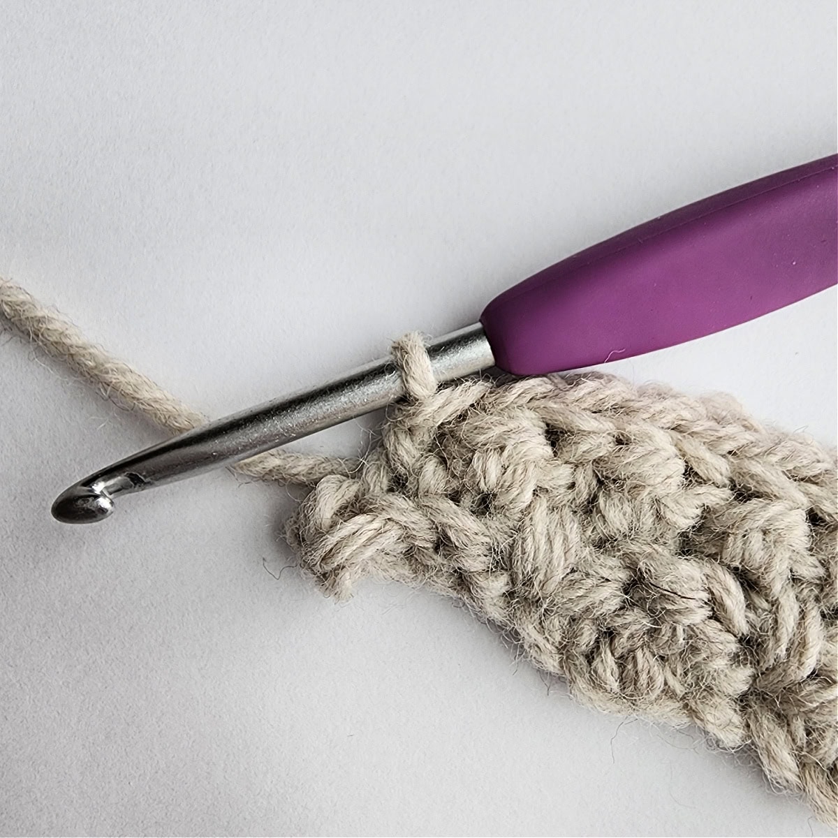 Row 4 of the crochet ornament with a purple crochet hook.