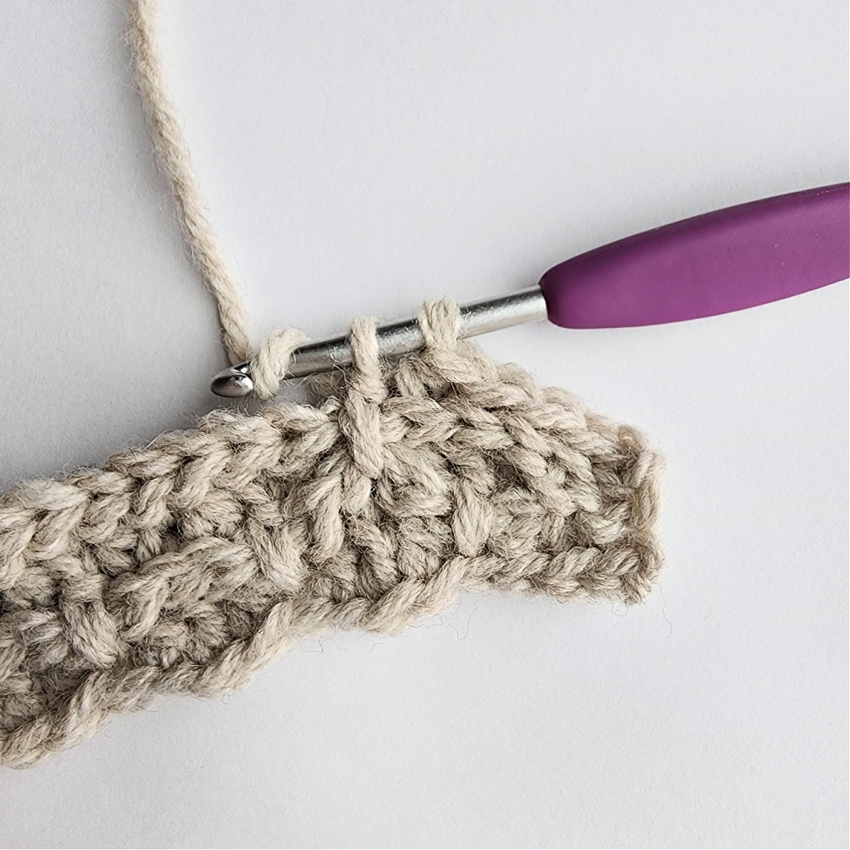Row 5 of the crochet ornament with a purple crochet hook.