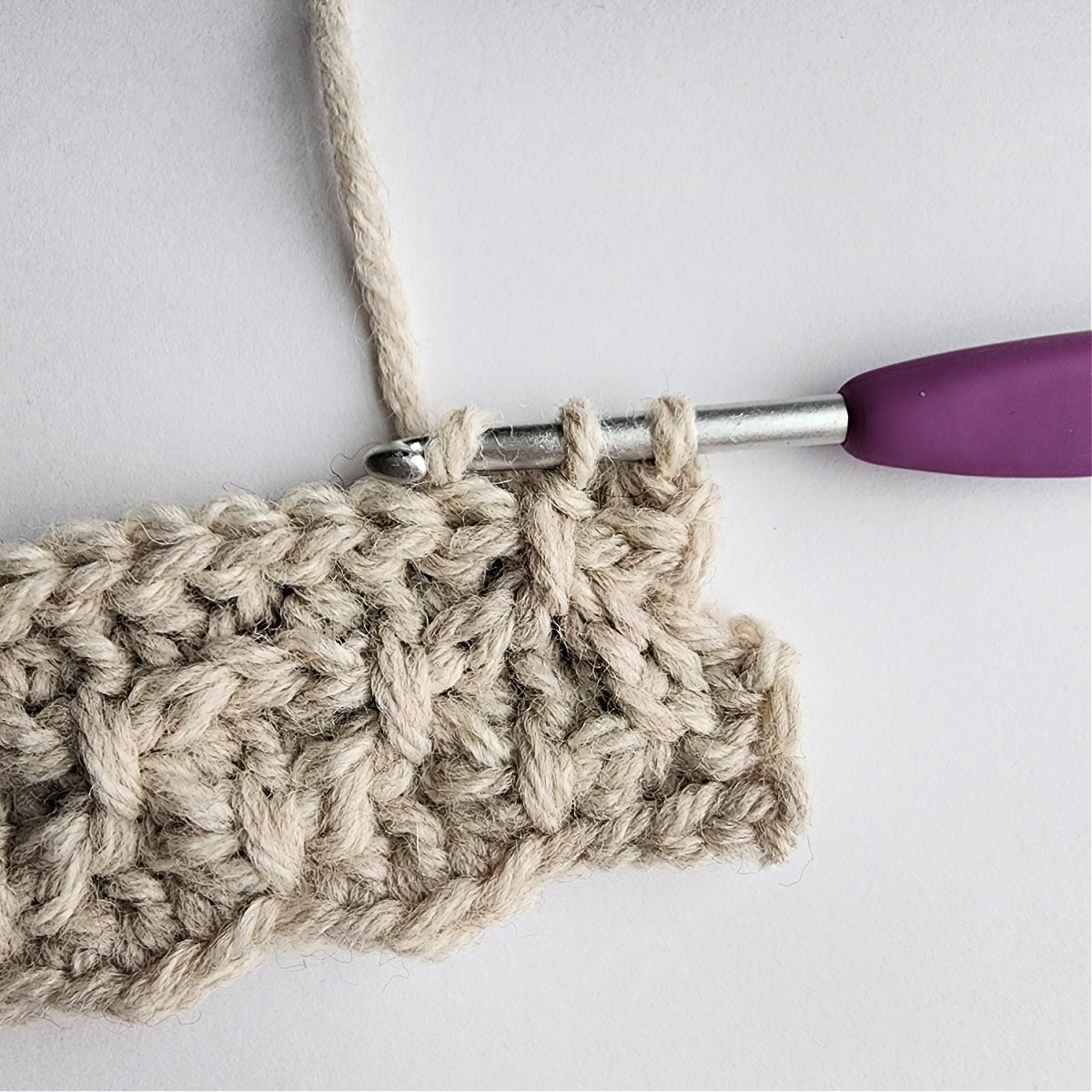 Row 7 of the crochet ornament with a purple crochet hook.