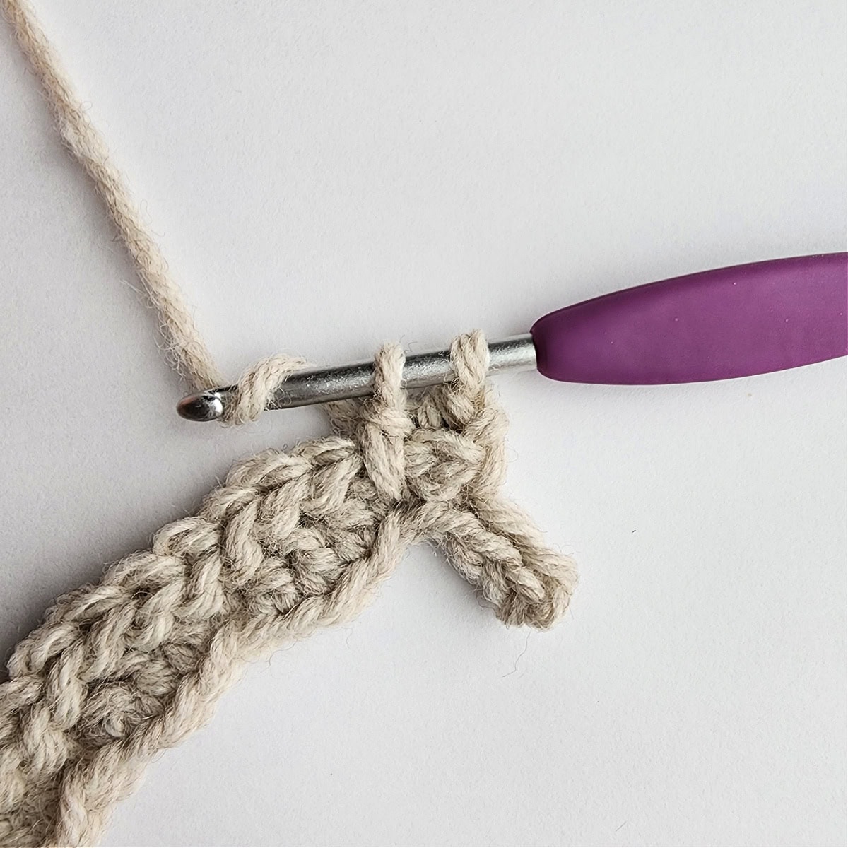 Row 3 of the crochet ornament with a purple crochet hook.