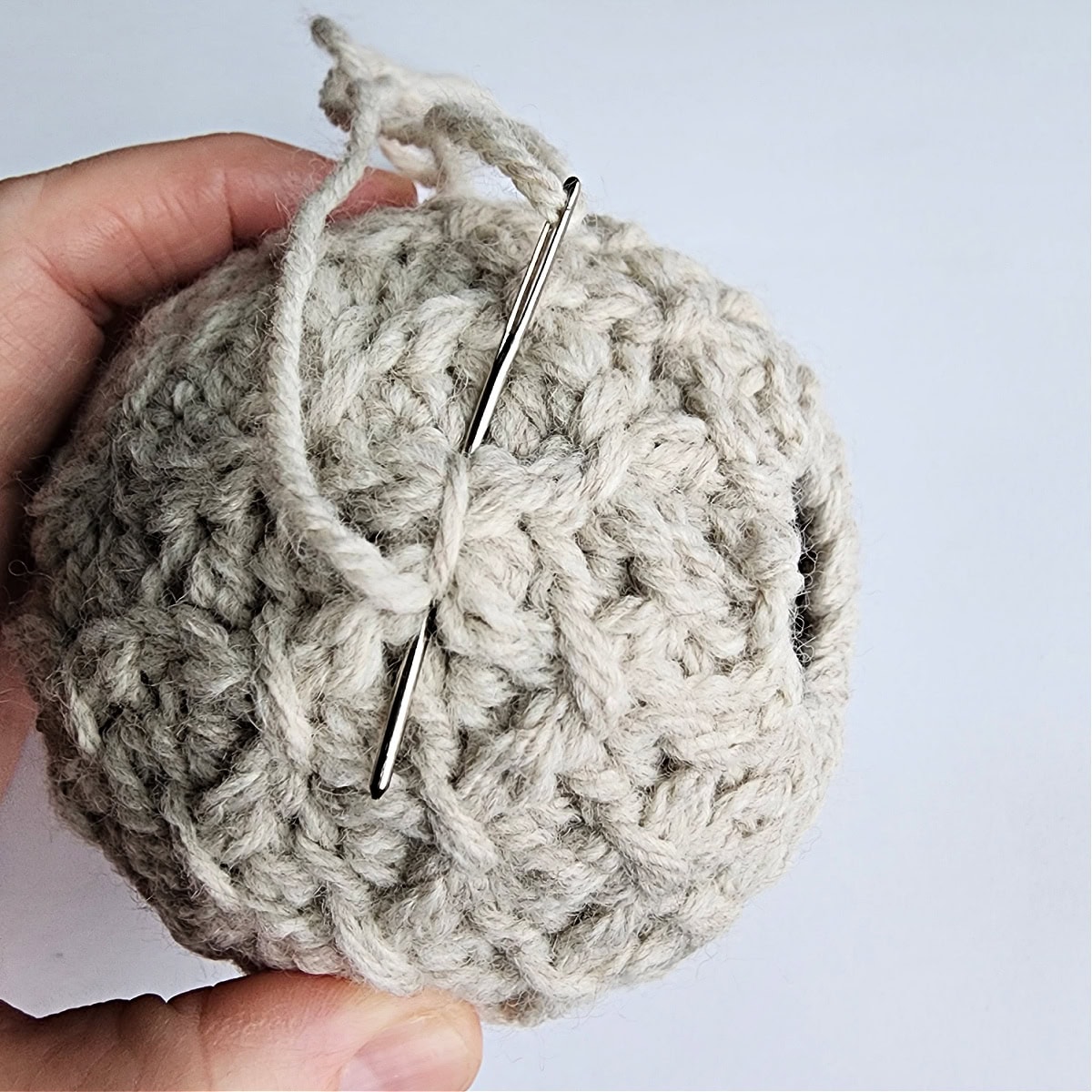 Thread and needle being used to tie the top of the crochet ornament.