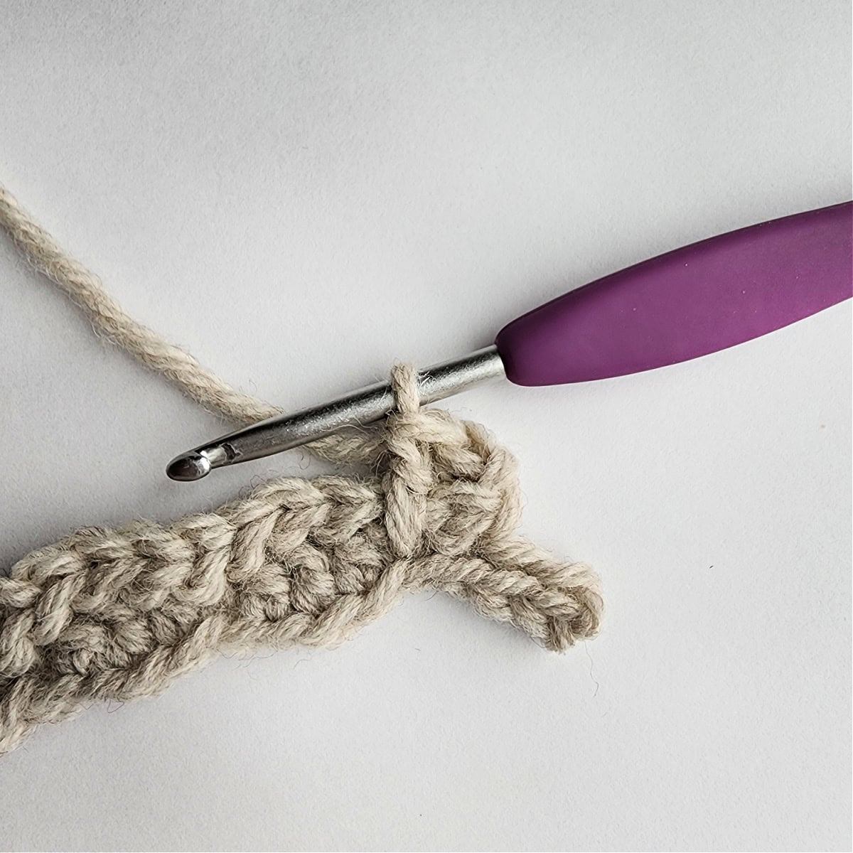 Row 3 of the crochet ornament with a purple crochet hook.