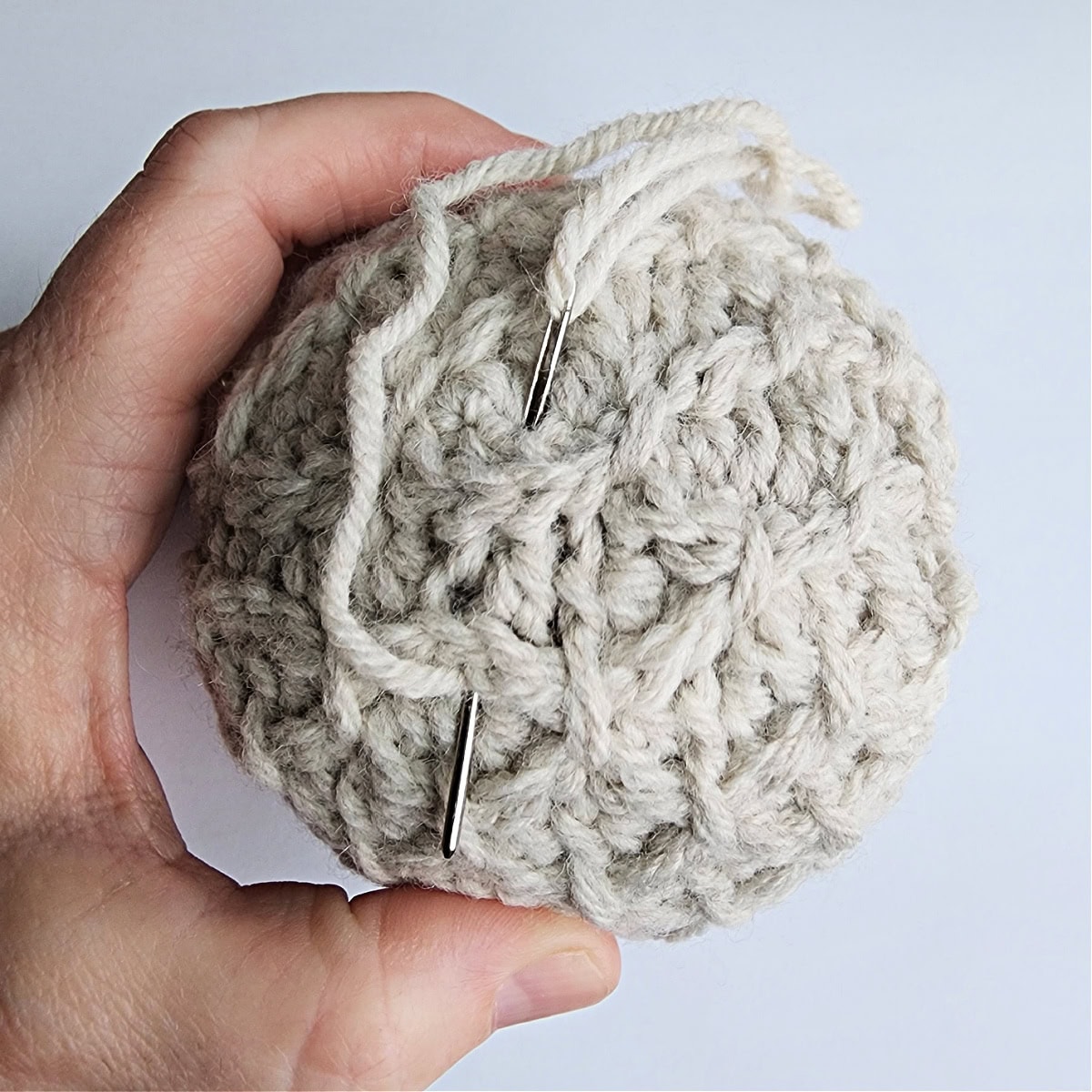 Thread and needle being used to tie the top of the crochet ornament.