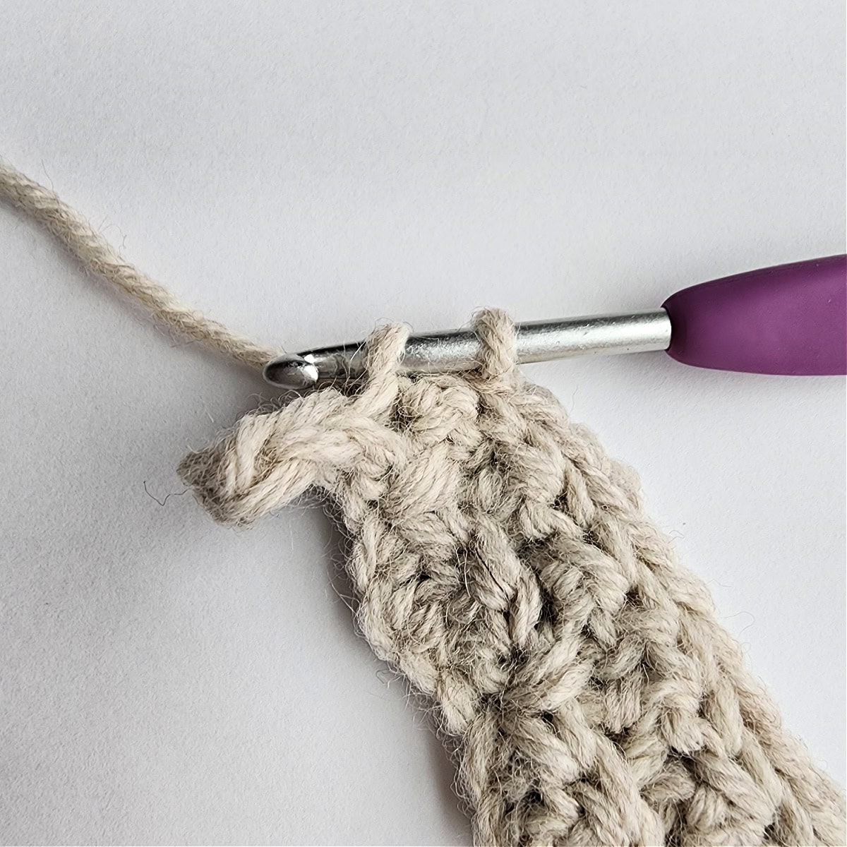 Row 4 of the crochet ornament with a purple crochet hook.