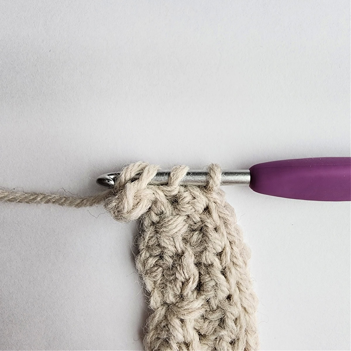 Row 4 of the crochet ornament with a purple crochet hook.