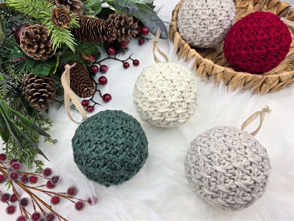 Close-up of five Christmas colored crochet baubles and holiday greenery.