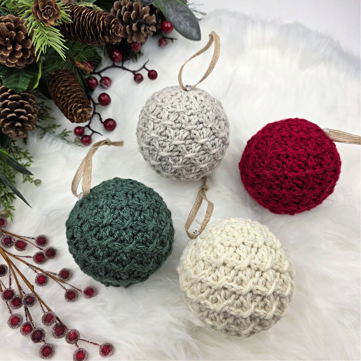 Knit-look crochet Christmas bauble laying on a faux fur rug with pinecones, berries, and greenery.