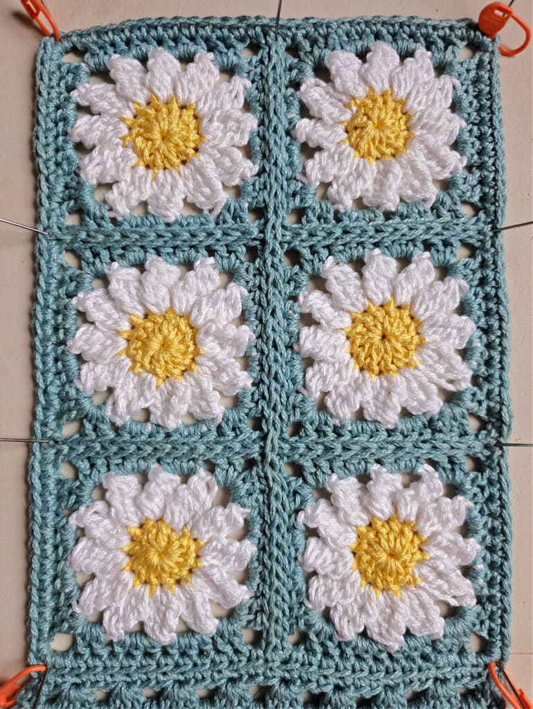 Blocking six crochet daisy granny squares which are seamed together.