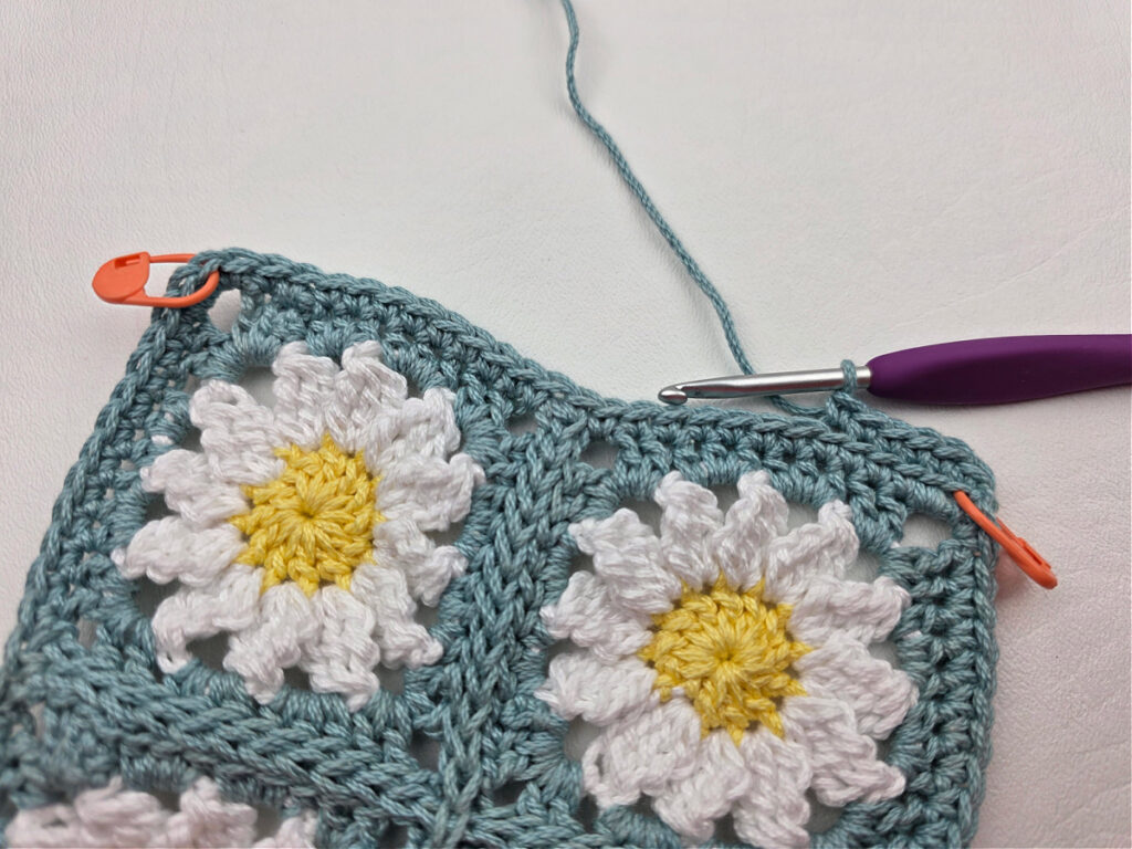 Working the border around two crochet daisy granny squares.