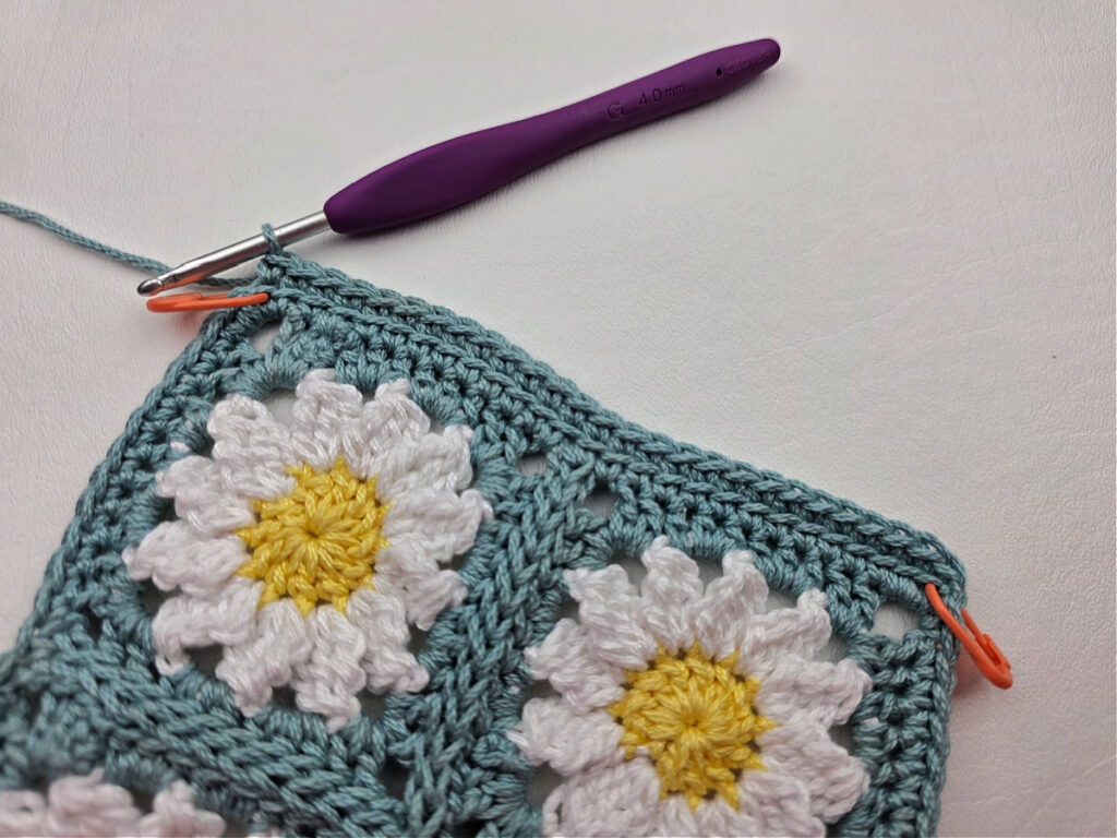 Working the border around two crochet daisy granny squares.