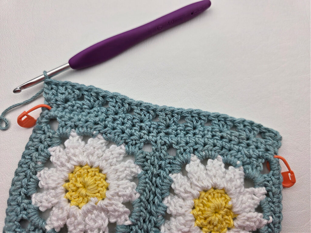 Working the border around two crochet daisy granny squares.