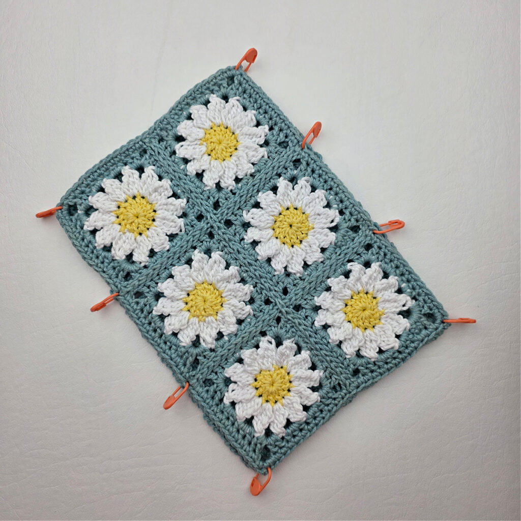 Six completed crochet daisy granny squares on a white surface with stitch markers.