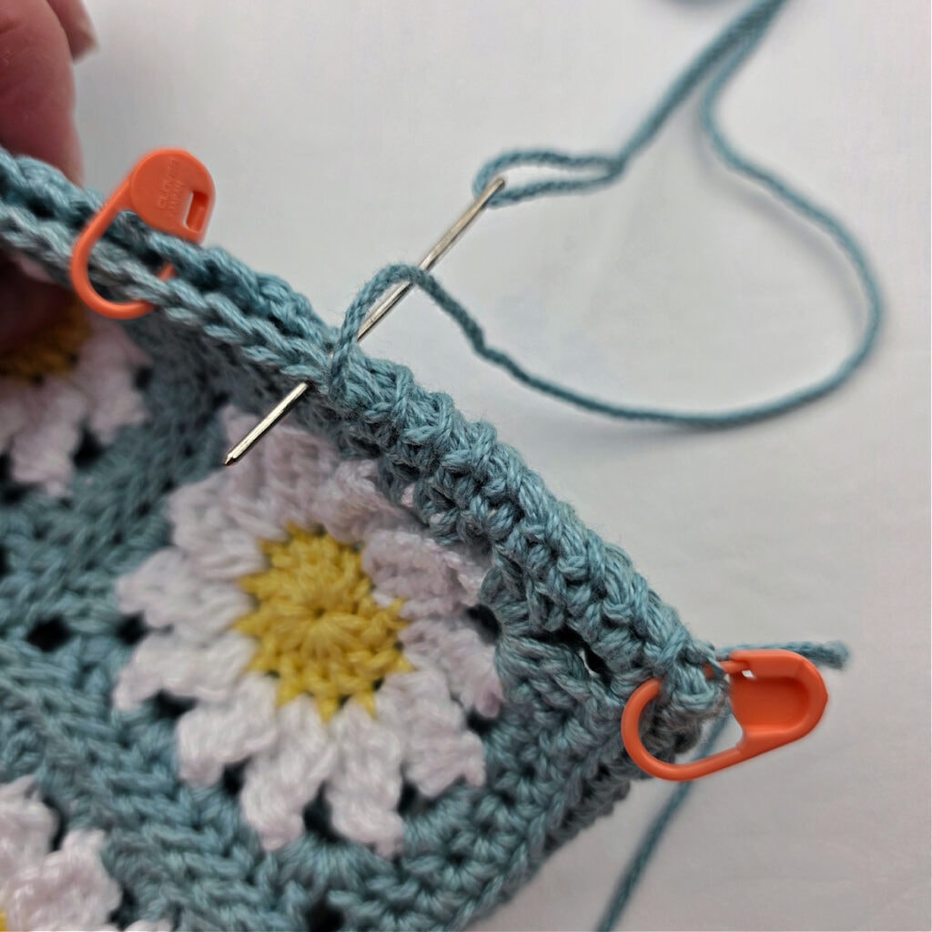 Seaming together a crochet daisy granny square pouch.