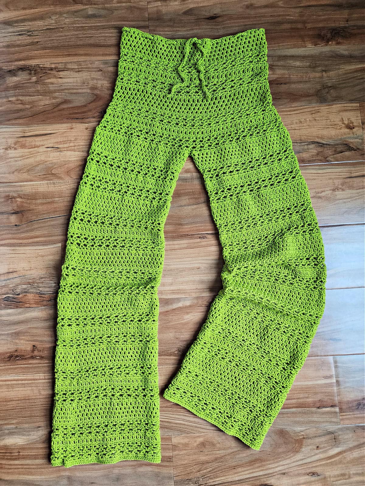 Green-colored lacy crochet pants against a wooden floor