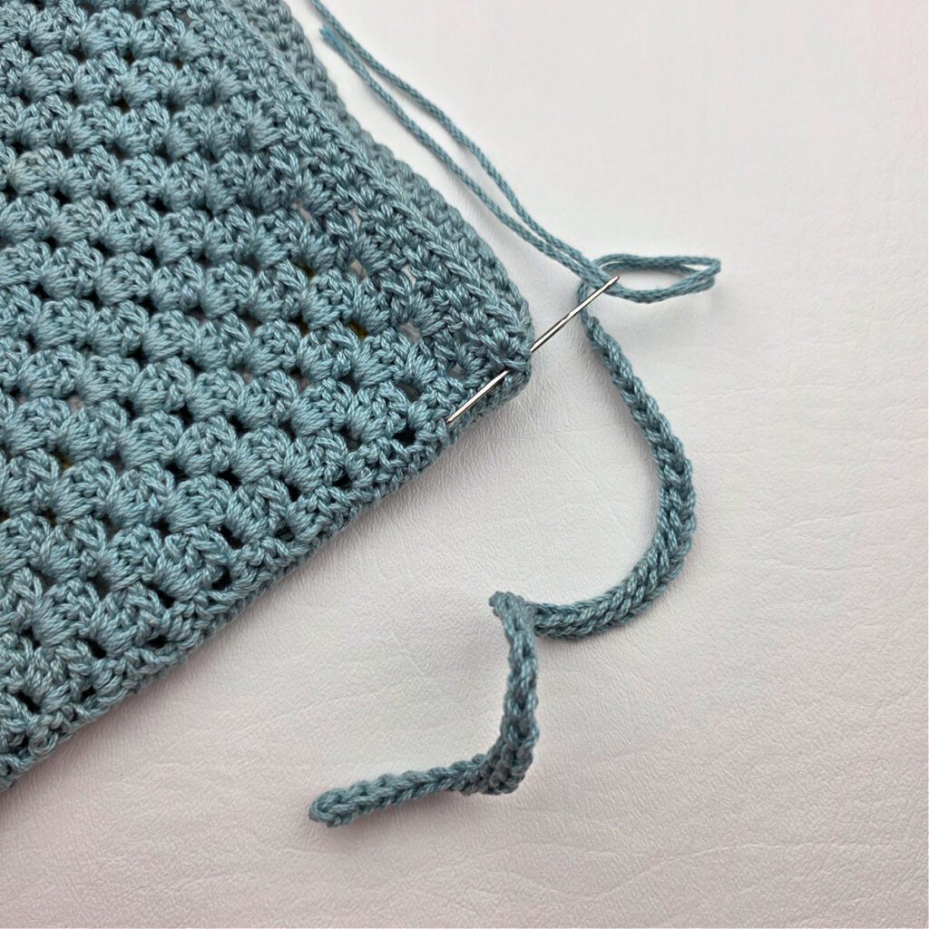 The edge of a teal colored crochet granny square pouch.
