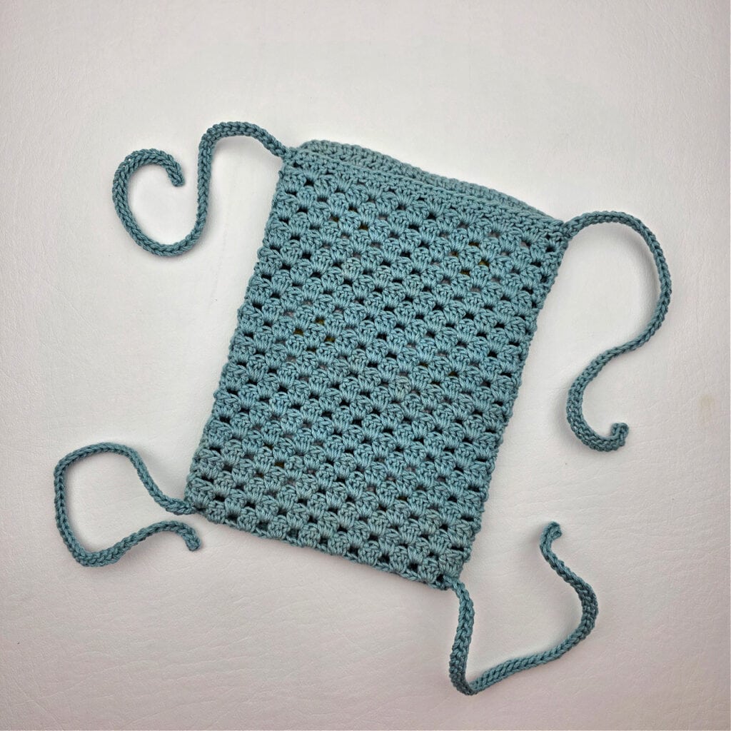 Teal colored crochet pouch with strings attached to it.