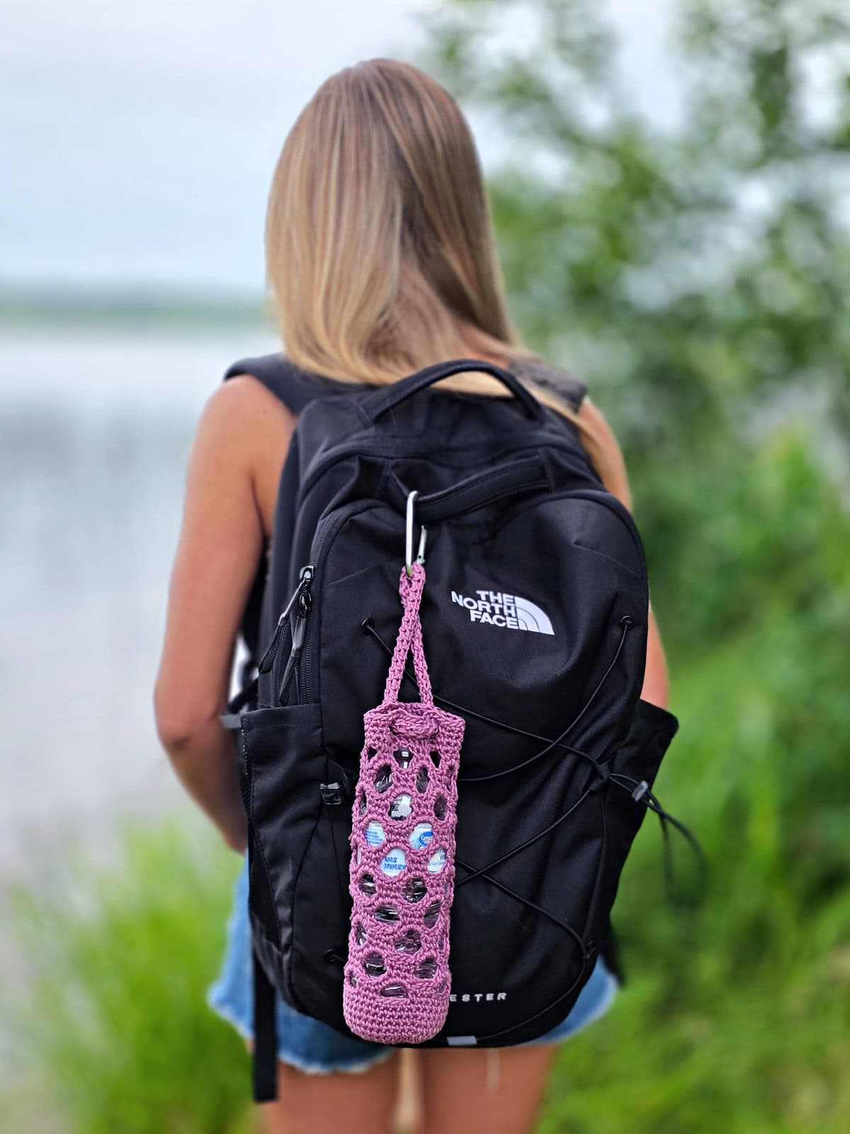 A girl standing with her back to the camera with a purple crochet water bottle holder attached to her backpack.
