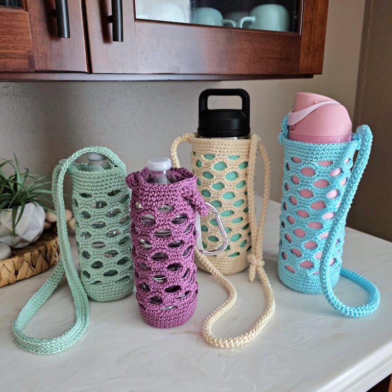 Green, purple, off-white, and blue colored crochet water bottle holders on a white counter.