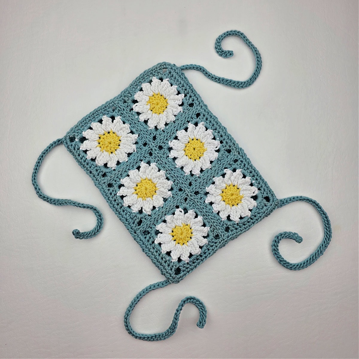 A crochet pouch made from six crochet daisy granny squares seamed together.