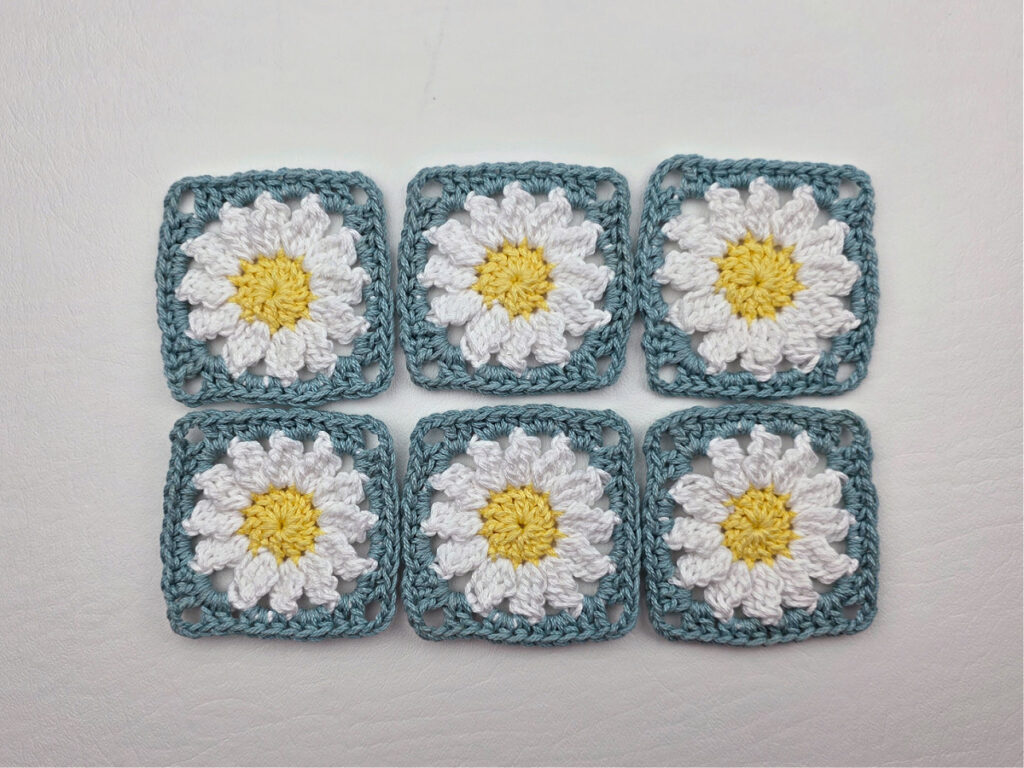 Six completed crochet daisy granny squares on a white surface.