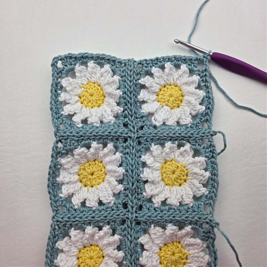 Six completed crochet daisy granny squares on a white surface.