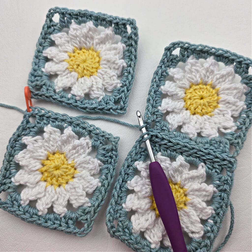 Seaming together four crochet daisy granny squares.