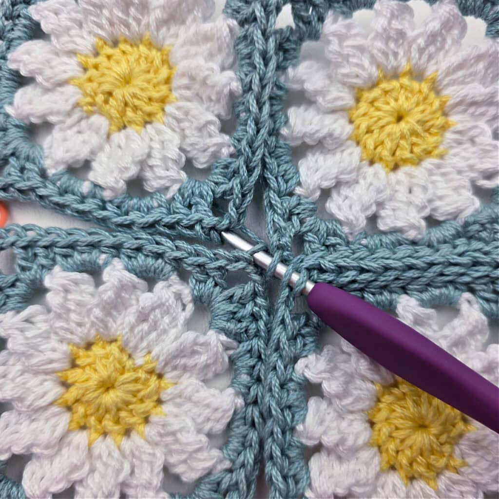 Seaming together four crochet daisy granny squares.