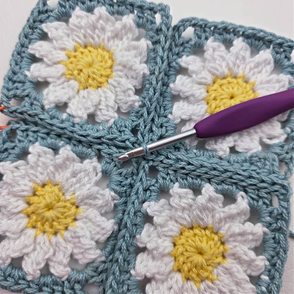 Seaming together four crochet daisy granny squares.
