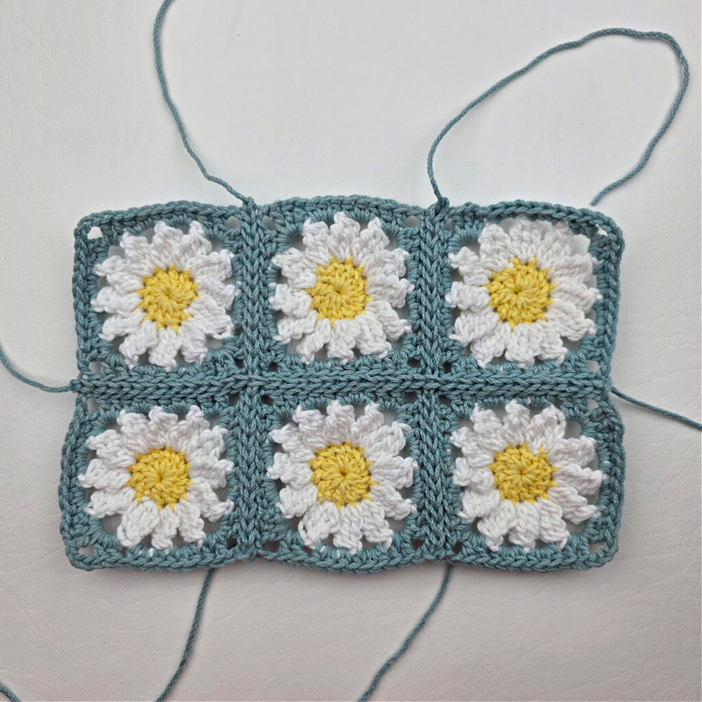 Six completed crochet daisy granny squares on a white surface.