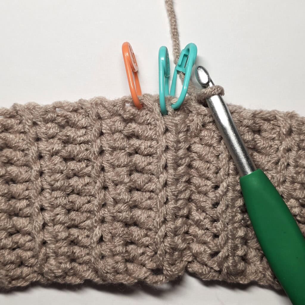 A crochet hook inserted in the crochet waistband with stitch markers attached to it.