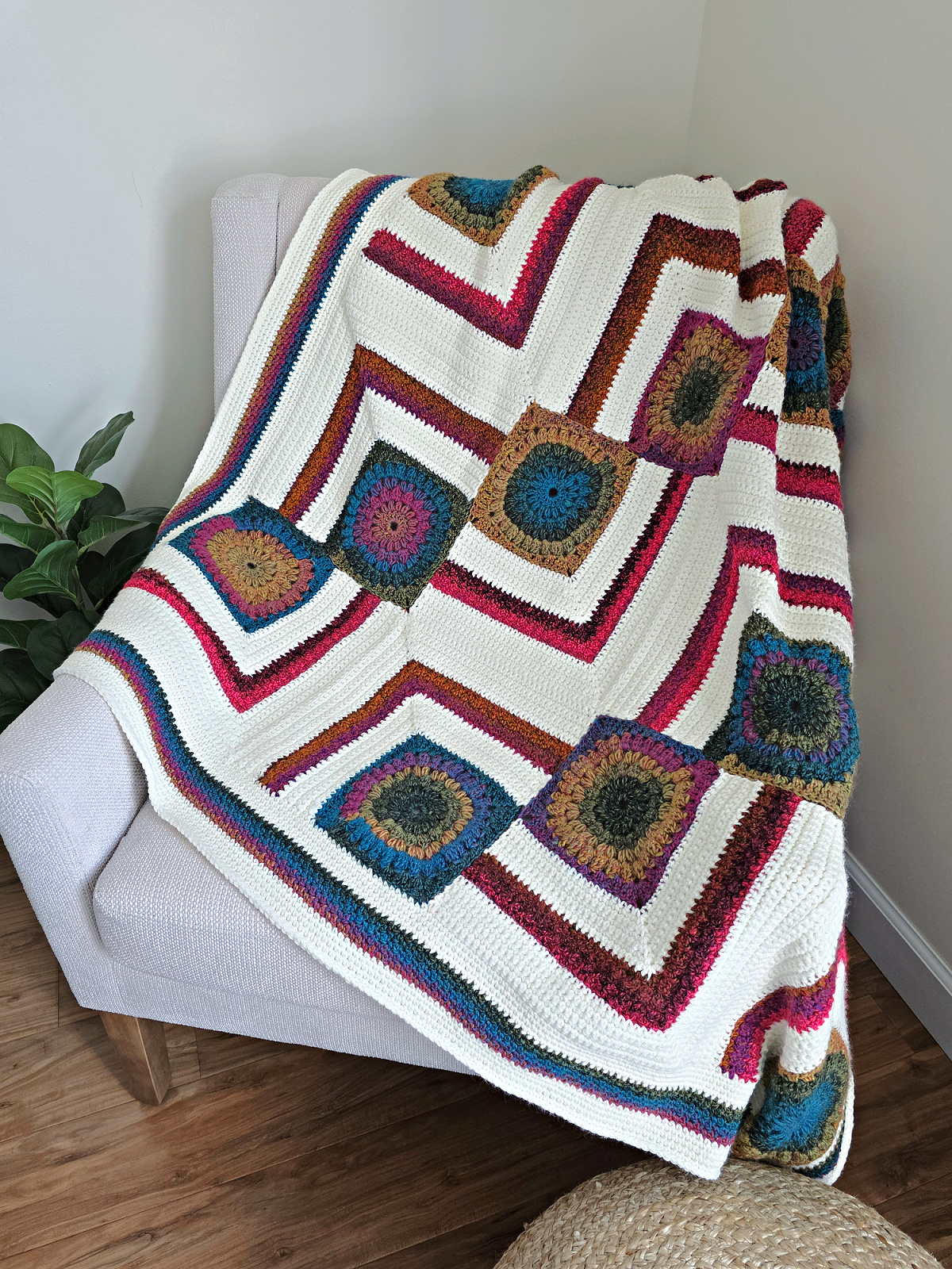 A colorful modern crochet blanket pattern free spread across a sofa with a plant next to it.