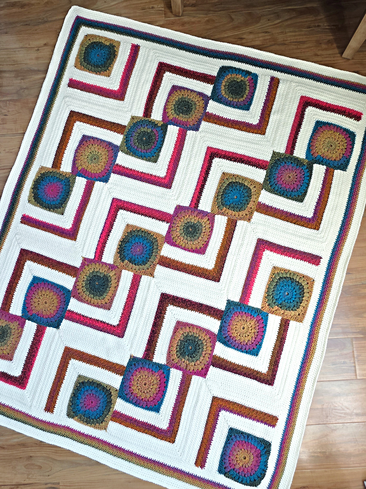 A colorful crochet blanket spread on the wooden floor.