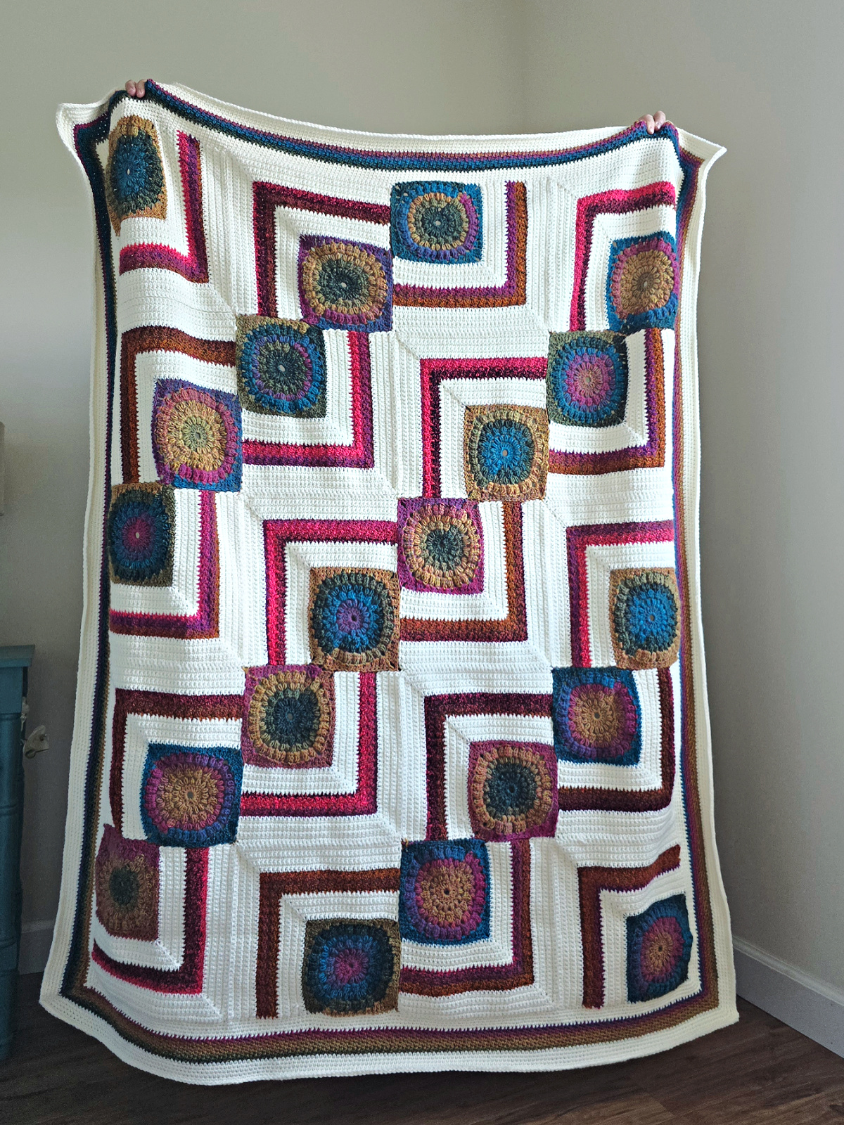 A colorful granny squares crochet blanket held up.