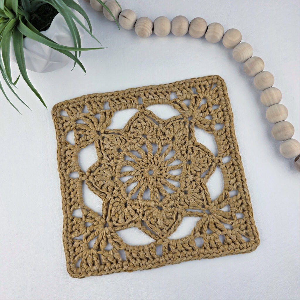 A brown granny square flower motif with a string of white beads laid out.