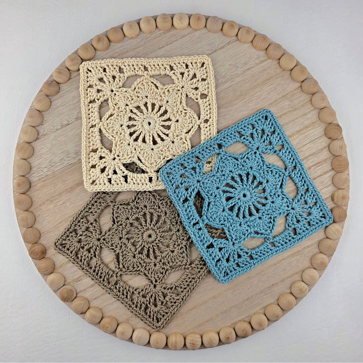 Blue, brown, and white colored granny square flower motifs laid out on a circular wooden tray.