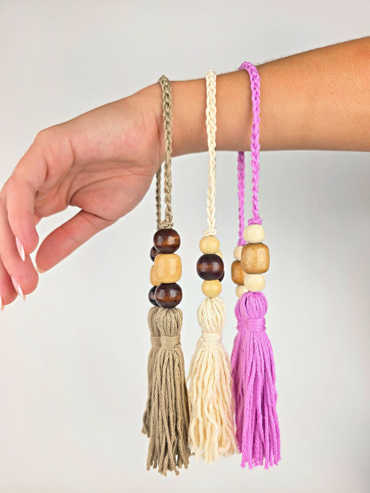 Three handmade yarn tassels with beads hanging over a wrist.