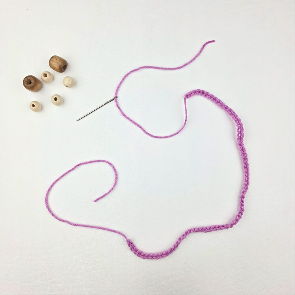 Wooden beads and a pink strand of yarn pulled through a yarn needle.